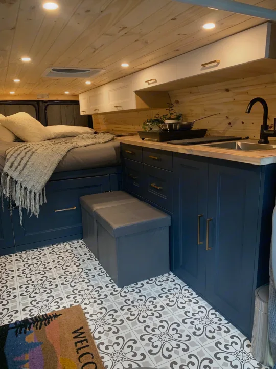 Explore this RV rental's chic interior: wood-paneled walls, dark blue kitchen, comfy bed, and patterned tile floor.. Ford E350 Box Van 2010