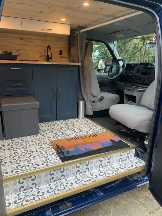 Cozy RV rental van interior: driver's cabin, stylish kitchenette with dark cabinets, and patterned floor tiles.. Ford E350 Box Van 2010