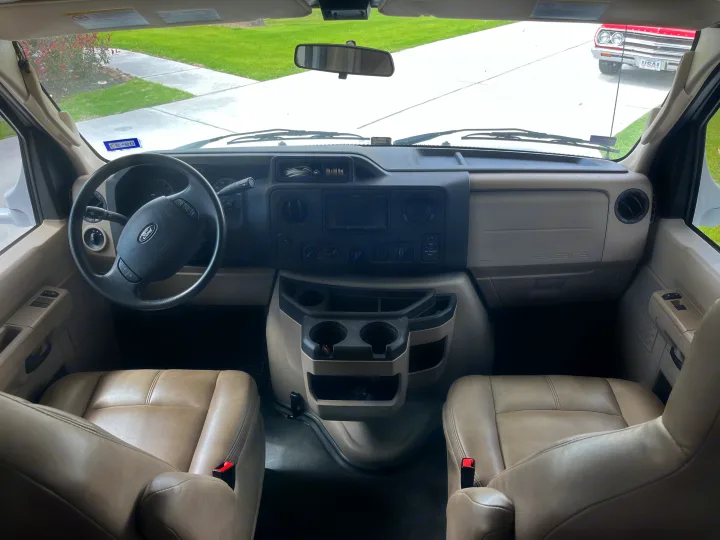 RV rental interior showing front cabin, dashboard, steering wheel, tan seats, and a classic car outside.. Thor Four Winds 2017
