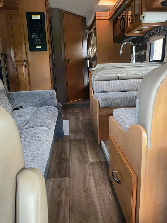 Inside an RV rental: a cozy space with sofa, dinette, kitchen, control panel, and wood-look flooring in a compact layout.. Thor Four Winds 2017