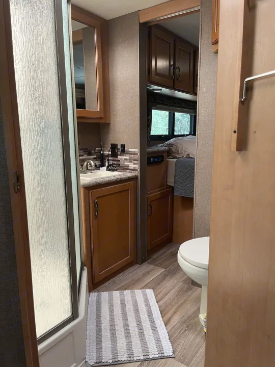 This rv rental features a compact bathroom with shower, sink, & toilet, leading to a cozy bedroom. Functional design for travel.. Thor Four Winds 2017