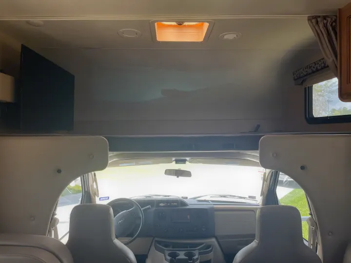 Inside a spacious RV rental, featuring the front cab, dashboard, steering wheel, TV, and overhead bunk.. Thor Four Winds 2017