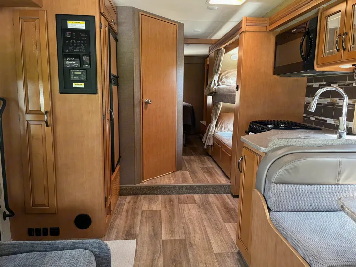 RV rental interior with modern wood cabinetry, compact kitchen, control panel, and bunk beds for comfortable travel.. Thor Four Winds 2017