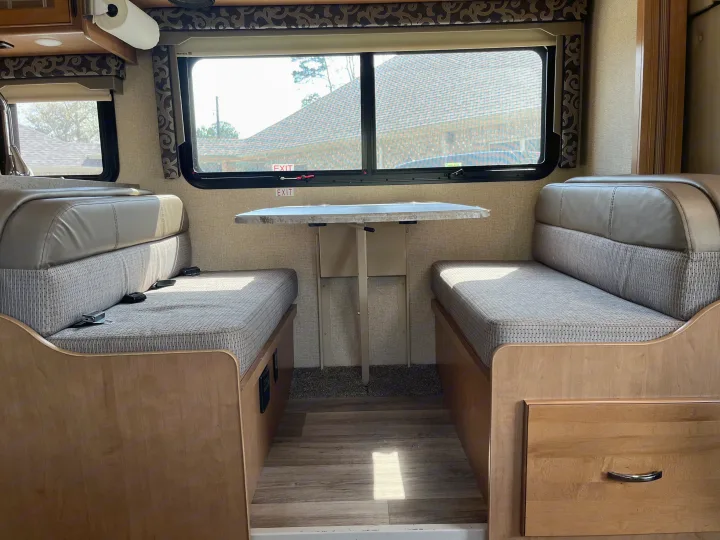 RV rental dinette with facing benches, a table, and large windows. The comfortable interior is ready for travel adventures.. Thor Four Winds 2017