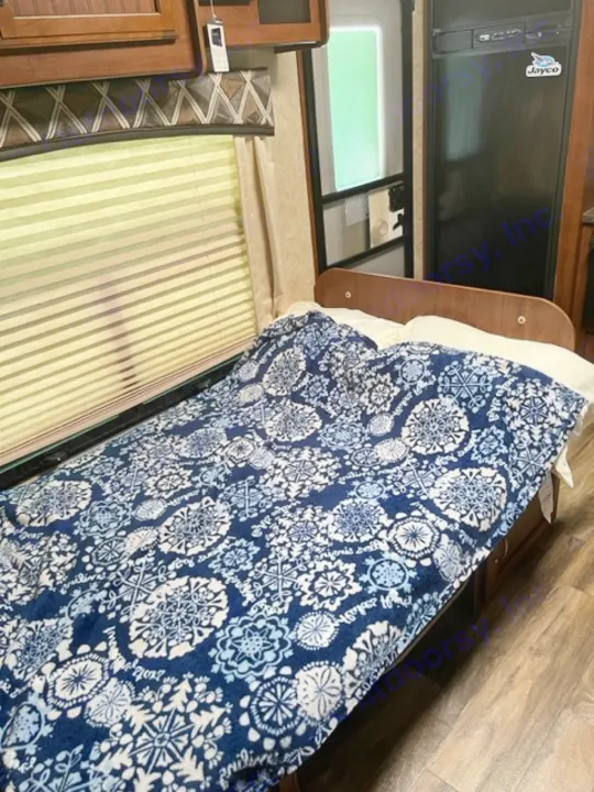 RV rental interior featuring a compact fridge, window, and a bed with a vibrant blue and white patterned blanket. Comfortable amenities.. Jayco White Hawk 2017