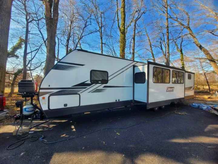 White travel trailer RV rental, featuring a slide-out and front grill setup, parked on asphalt under a clear sky.. Dutchmen Coleman Light 2021