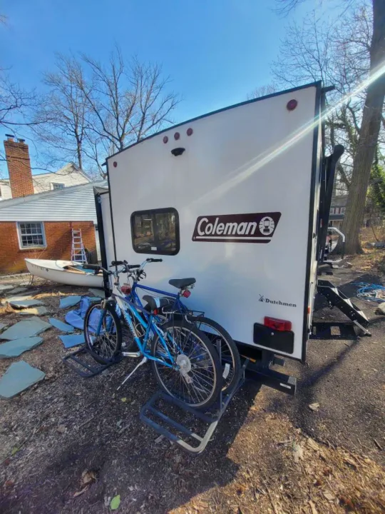 White Coleman RV rental with two bikes mounted on the rear rack, parked outdoors, ready for your next adventure.. Dutchmen Coleman Light 2021