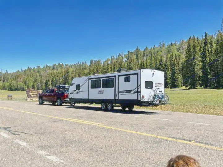 Explore nature with this RV rental! A truck tows a large travel trailer with bikes on a scenic forest road.. Dutchmen Coleman Light 2021