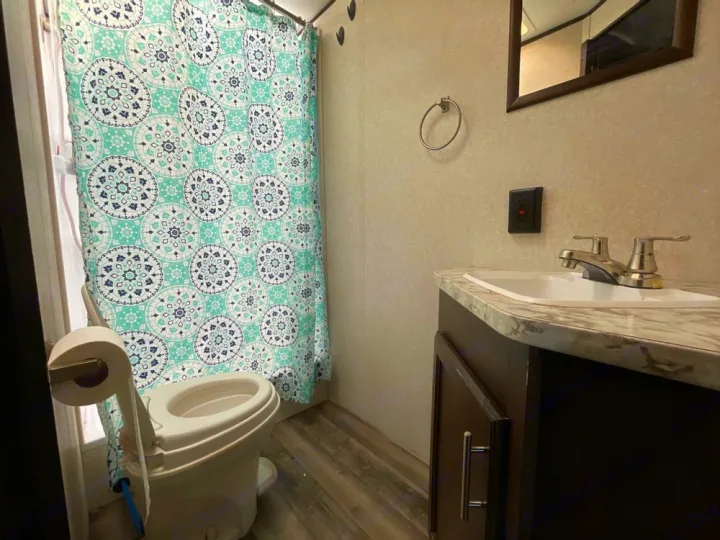 Clean RV rental bathroom featuring a toilet, patterned shower curtain, and vanity with sink & mirror.. Jayco Jay Flight SLX 2019