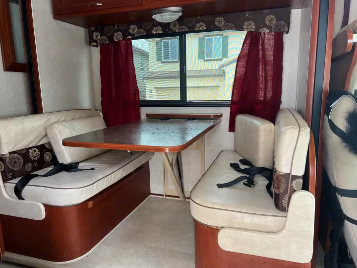 This inviting RV rental interior features a cozy dinette with cream benches, a table, and a window with red curtains.. Winnebago Minnie Winnie 2015