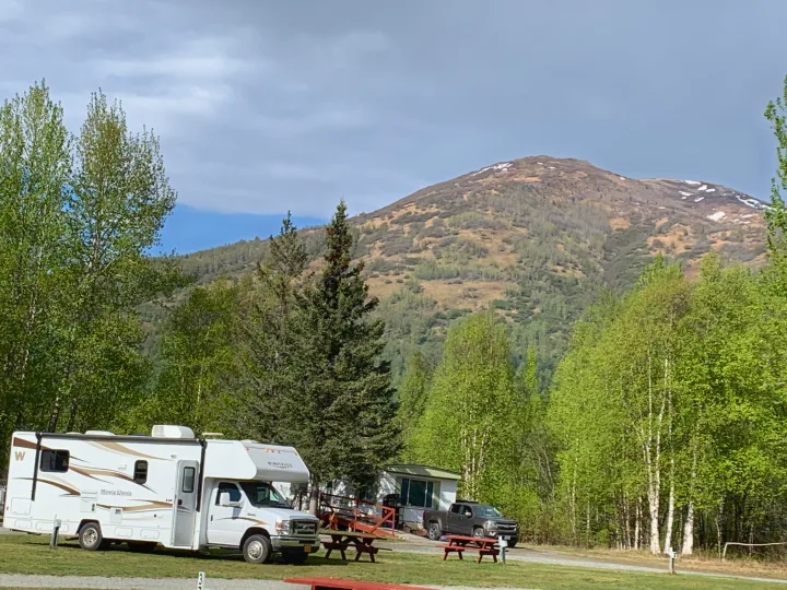 An RV rental is parked at a scenic mountain campground amidst green trees and patches of snow.. Winnebago Minnie Winnie 2015