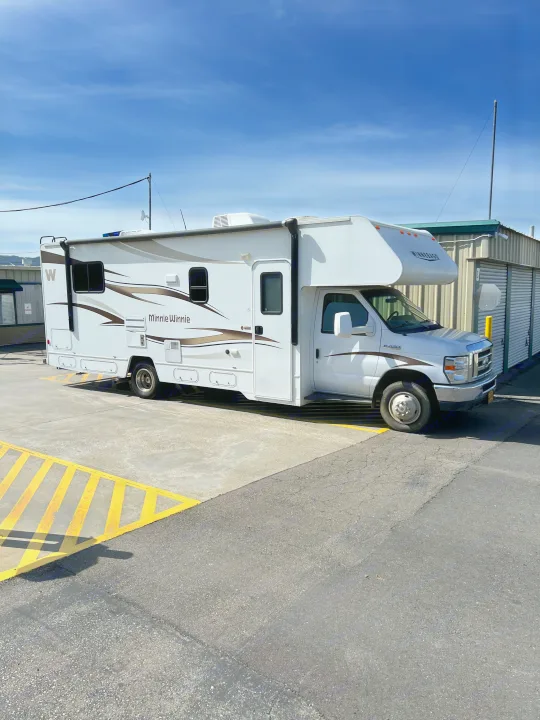 A large white Winnebago Minnie Winnie RV is parked on pavement next to storage units, possibly for rv rental.. Winnebago Minnie Winnie 2015