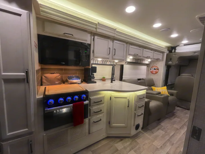 Well-lit, modern RV kitchen with white cabinets, blue-lit stove, and comfy seating. Perfect for your next rv rental adventure.. Entegra Coach Vision 29S 2022