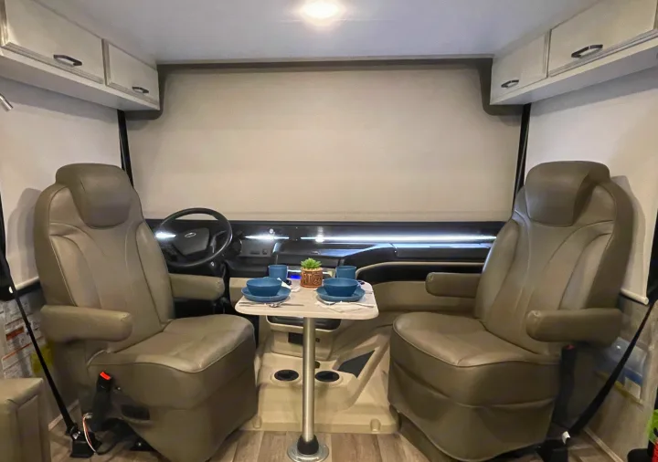 RV rental interior shows swiveling captain's chairs and a small dining table set for two, offering comfort in this motorhome cockpit.. Entegra Coach Vision 29S 2022