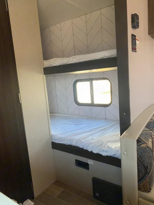 Experience comfort in our RV rental! Cozy bunk beds with a stylish geometric wall and a sunny window, ideal for camping.. Keystone Springdale 1800BH 2019