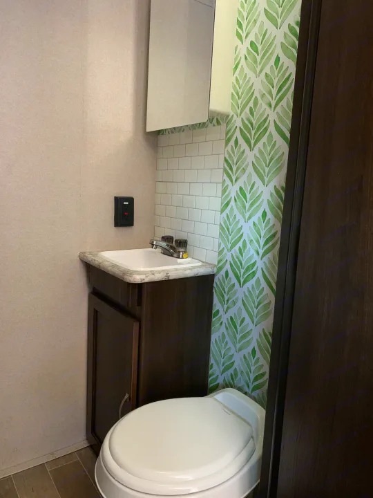 Compact RV rental bathroom with a small sink, vanity, toilet, subway tile, and green leaf wallpaper.. Keystone Springdale 1800BH 2019
