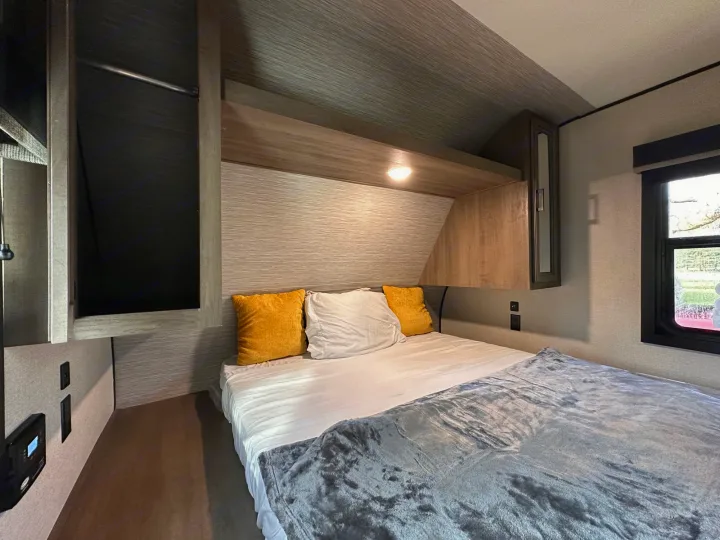 RV rental bedroom with comfortable bed, yellow and white pillows, overhead storage, closet space, and a window.. Highland Ridge RV Olympia 2022