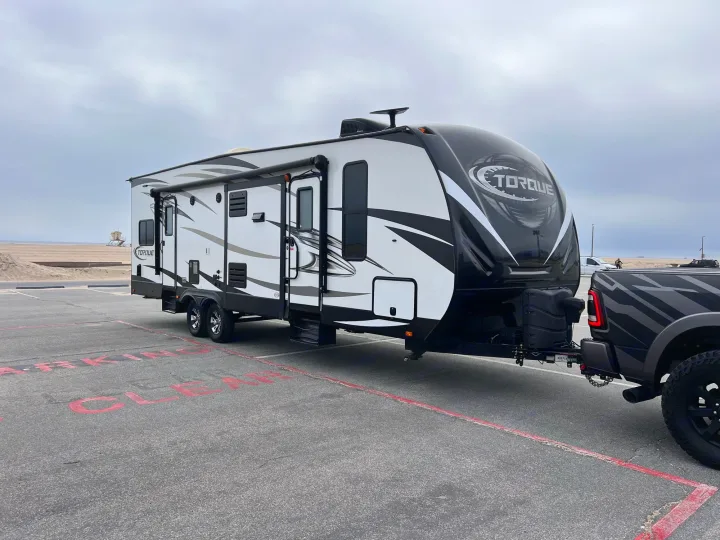 Large white and black Torque travel trailer hitched to a pickup truck in a beach parking lot. Ideal for your next rv rental trip.. Other Other 2017