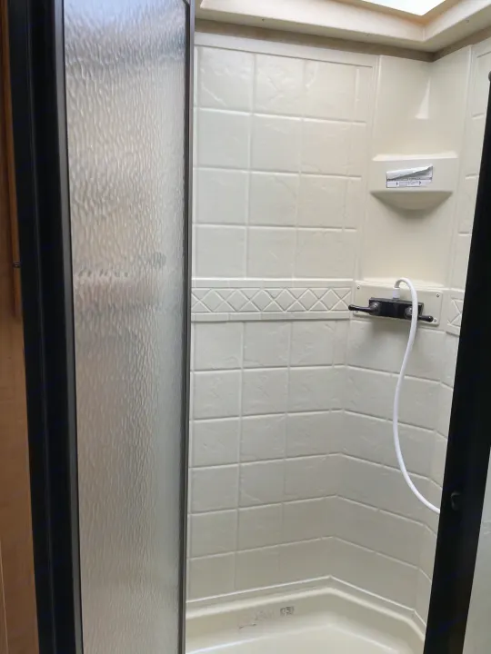 RV rental shower: compact stall with off-white, tile-look walls, textured glass door, and faucet with hose.. Damon Corporation Challenger 2009