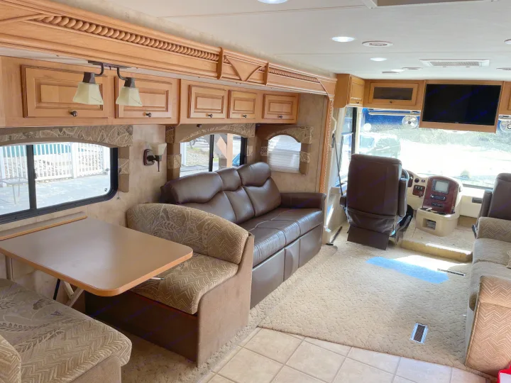 Inside an rv rental: a cozy living space with a dinette, leather sofa, and driving area. Features wood cabinets & large windows.. Damon Corporation Challenger 2009