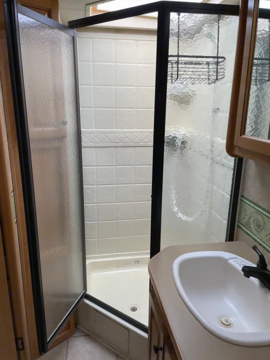 Compact RV rental bathroom featuring a stand-up shower with frosted glass enclosure and white tiled walls, plus a small sink.. Damon Corporation Challenger 2009