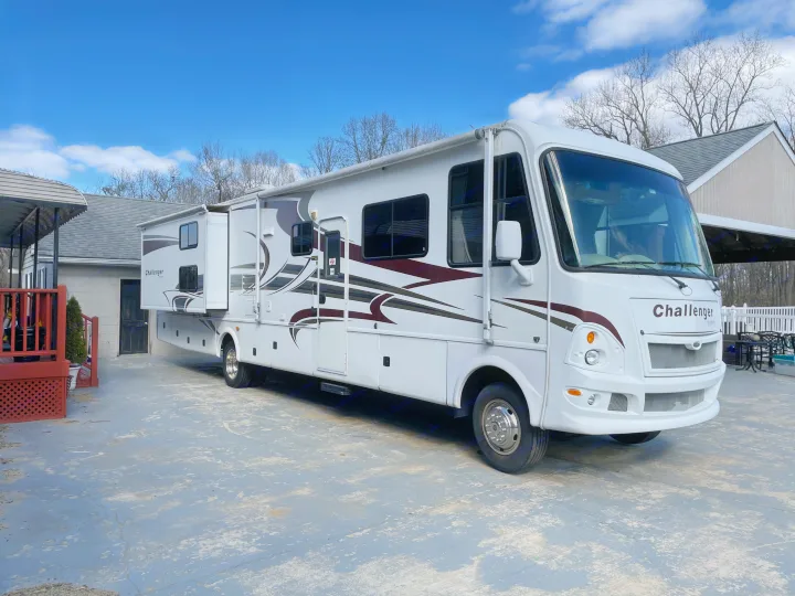White Challenger RV rental with slide-outs extended, parked on a paved driveway under a blue sky with clouds.. Damon Corporation Challenger 2009