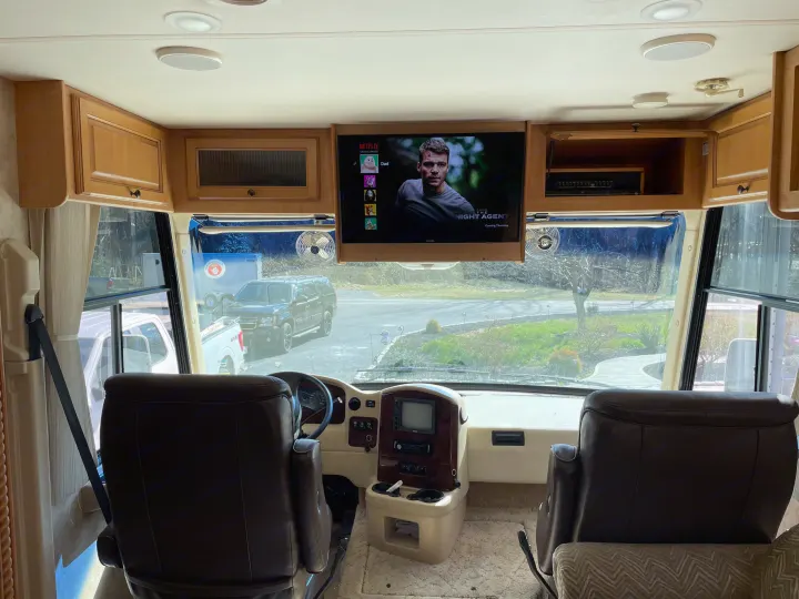 Inside an RV rental, the front driver's area features a TV playing Netflix, dashboard, and a view of the outside.. Damon Corporation Challenger 2009