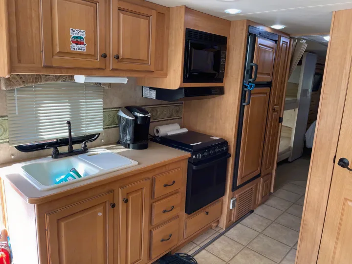 RV rental kitchen: light wood cabinets, sink, microwave, stove, and fridge, ideal for compact camper living.. Damon Corporation Challenger 2009
