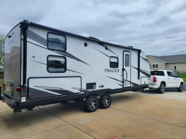 White travel trailer RV rental on a driveway, hitched to a pickup truck, ready for your next adventure.. Forest River Tracer 2022