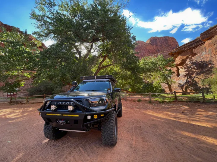 Rugged black Toyota 4Runner, an ideal RV rental for off-road adventures, parked by vibrant trees & stunning red rock cliffs.. Toyota 4Runner 2013