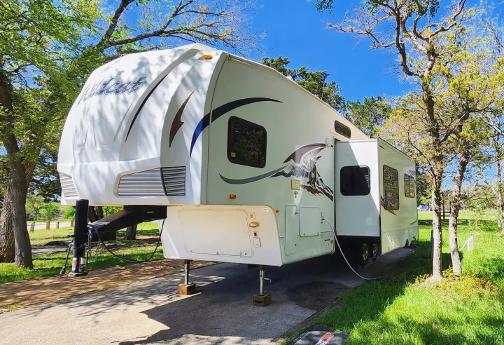 A white Wildcat fifth-wheel RV, ideal for an RV rental, is set up at a sunny treed campsite.. Forest River Wildcat 2008