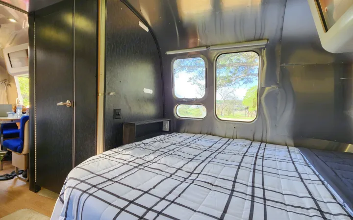 Experience RV rental comfort: a cozy bedroom features plaid bedding, iconic metallic walls, and bright outdoor views.. Airstream International 2004