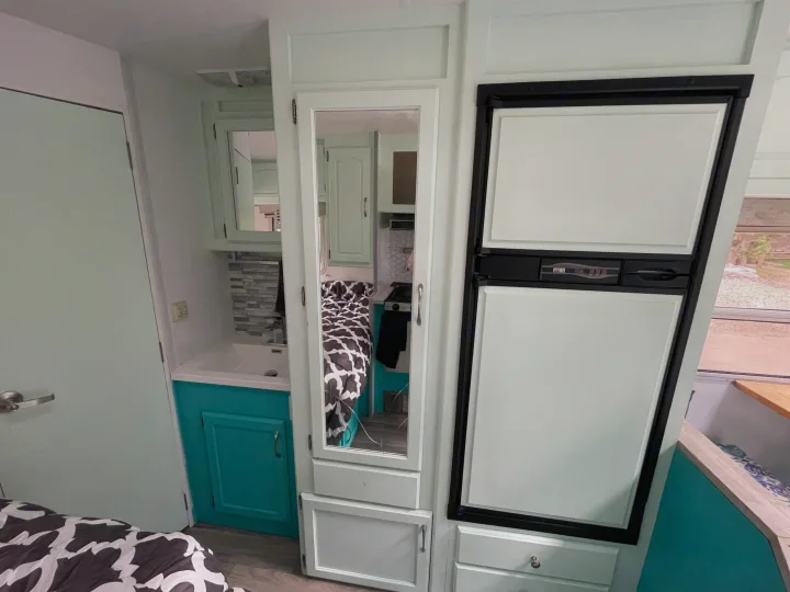 Stylish RV rental interior showcasing a mint green and turquoise living space with a bedroom, sink, and fridge.. Other Other 2005