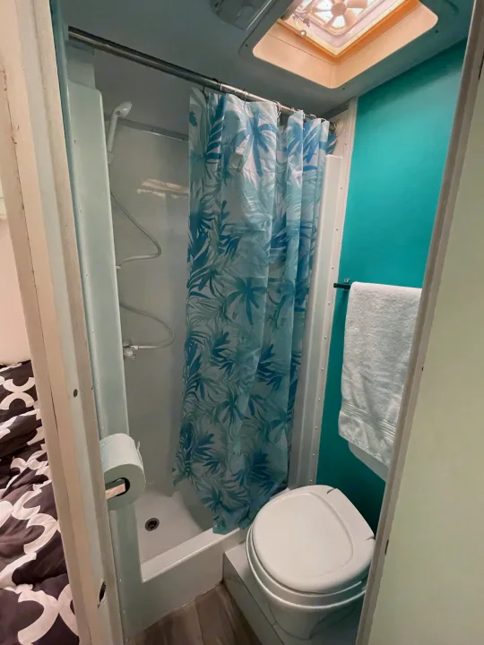 RV rental wet bath with blue leaf shower curtain, toilet, white towel on teal wall, and roof vent.. Other Other 2005