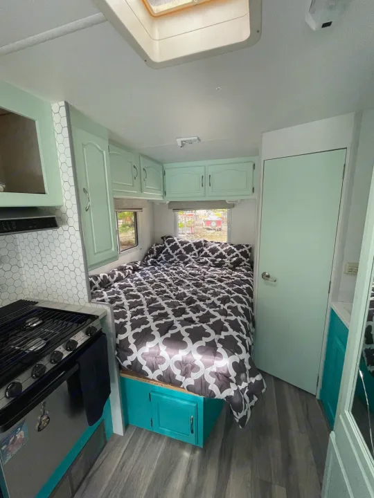 Bright RV rental interior: A bed with patterned comforter, mint green cabinets, and a white hexagon kitchen backsplash.. Other Other 2005