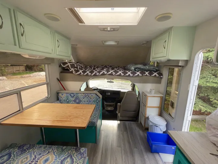 Inside a bright RV rental: features light green cabinets, a wooden dinette with blue patterned cushions, and an overhead bunk.. Other Other 2005