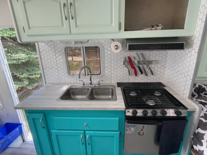 Bright and functional RV rental kitchen with mint and teal cabinets, modern hex tile backsplash, sink, and stove.. Other Other 2005