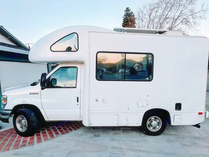 White, custom-built RV rental parked outdoors. Features an aerodynamic front cap & roof-mounted solar panels.. Four Winds Majestic 2010