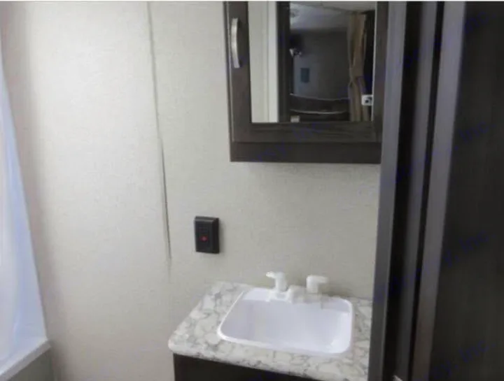 Compact RV rental bathroom features a vanity, sink with white faucets, mirrored cabinet, and shower area.. Keystone RV Springdale 2019
