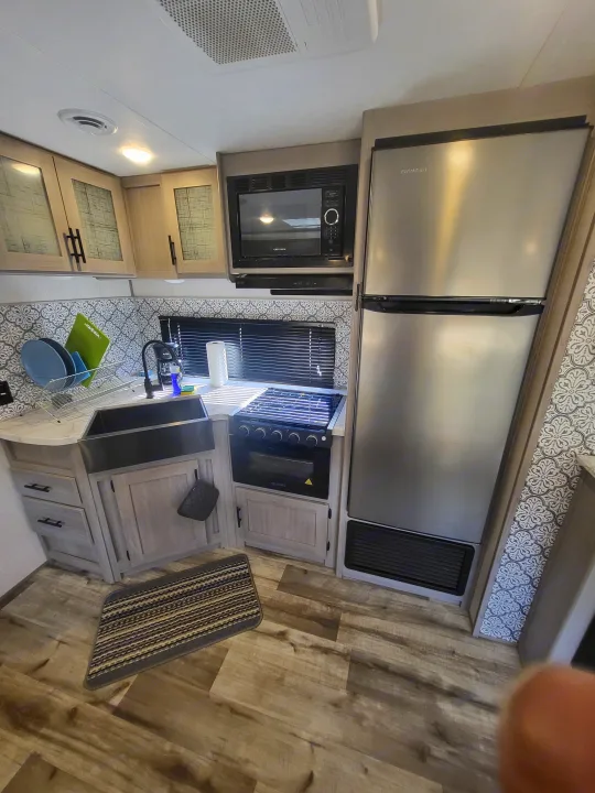 Modern RV rental kitchen interior, featuring a stainless steel fridge, microwave, and oven/stove combo.. Dutchmen 285BH 2022