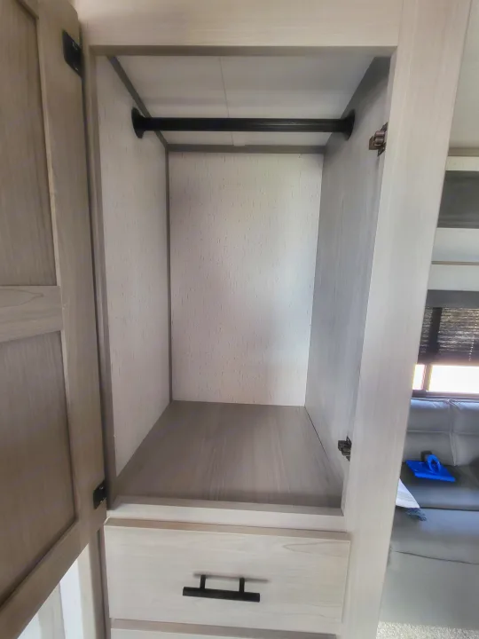 Spacious light wood interior storage in an RV rental, featuring an open cabinet with a black support pole.. Dutchmen 285BH 2022