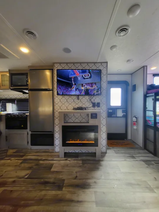 Spacious RV rental interior with a large TV, electric fireplace, full kitchen appliances, and wood floors.. Dutchmen 285BH 2022
