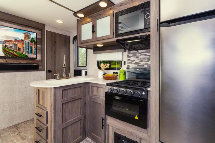 Modern RV rental interior with a fully equipped kitchen featuring a TV, sink, microwave, stove, and stainless steel fridge.. Gulf Stream 268BHS 2023