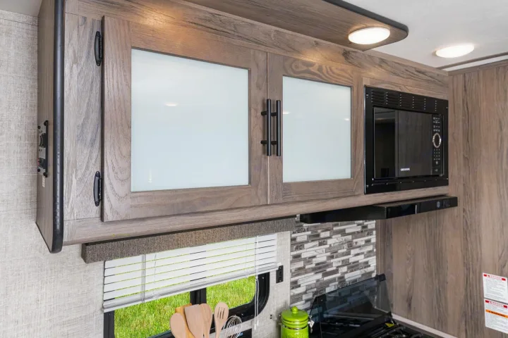 RV rental kitchen with stylish wood-grain cabinets, frosted glass doors, and built-in microwave, offering ample storage for your journey.. Gulf Stream 268BHS 2023