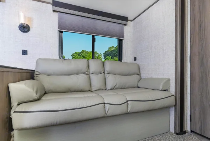 Inside this RV rental, a light gray sofa bed sits by a window with a green outdoor view, offering comfort and relaxation.. Gulf Stream 268BHS 2023