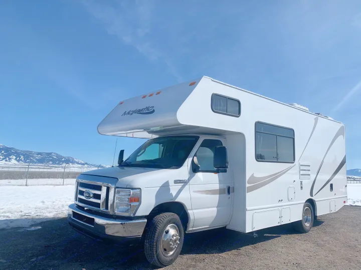 White Ford E350 Class C Majestic RV rental, parked with snowy mountains and clear blue sky. Ideal for winter travel.. Thor Freedom Elite 2019