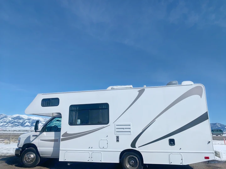 Spacious white RV rental parked against a clear blue sky and snow-capped mountains, ideal for travel.. Thor Freedom Elite 2019