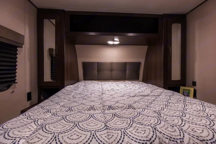 Cozy RV rental bedroom featuring a patterned bed, padded headboard, and built-in storage, perfect for comfortable travel.. Grand Design Transcend Xplor 265BH 2022