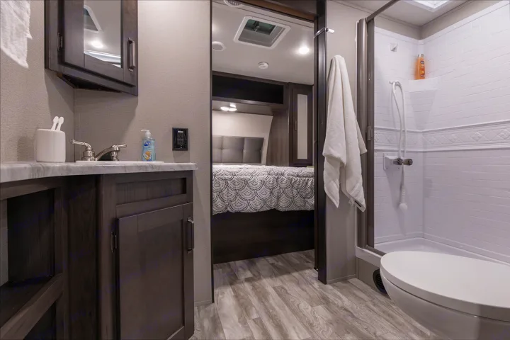 This RV rental showcases a compact bathroom with sink, mirror, shower, and toilet, leading to a comfortable bedroom.. Grand Design Transcend Xplor 265BH 2022