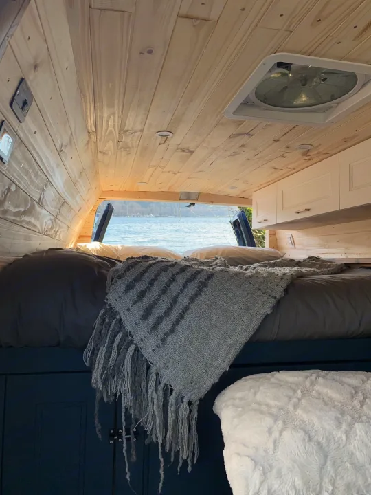 RV rental interior: wood-paneled walls, ceiling fan, cozy bed, and tranquil water view from the rear.. Ford E350 Box Van 2010